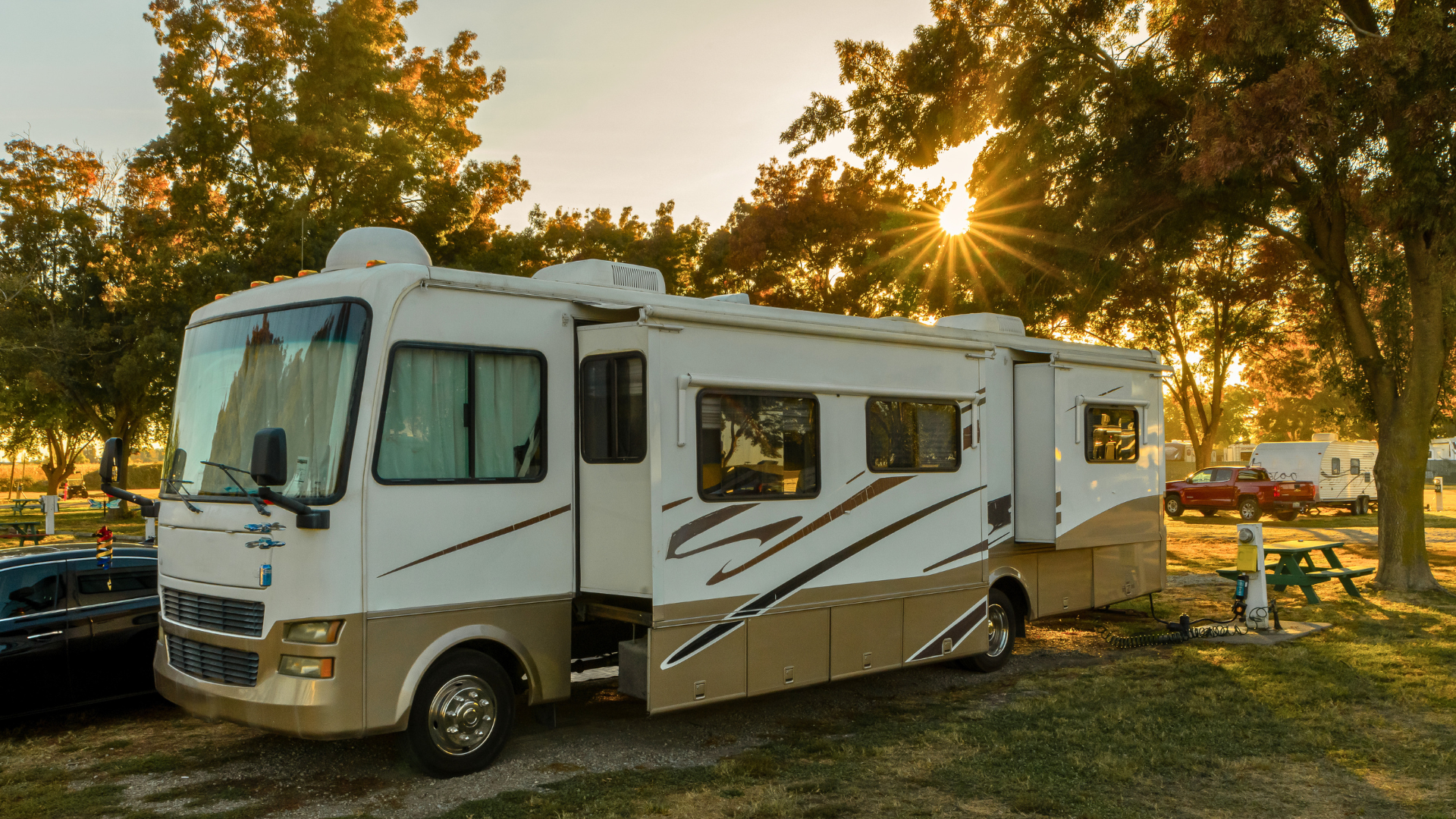 A white and tan recreational vehicle parked on a grassy campground at sunset.