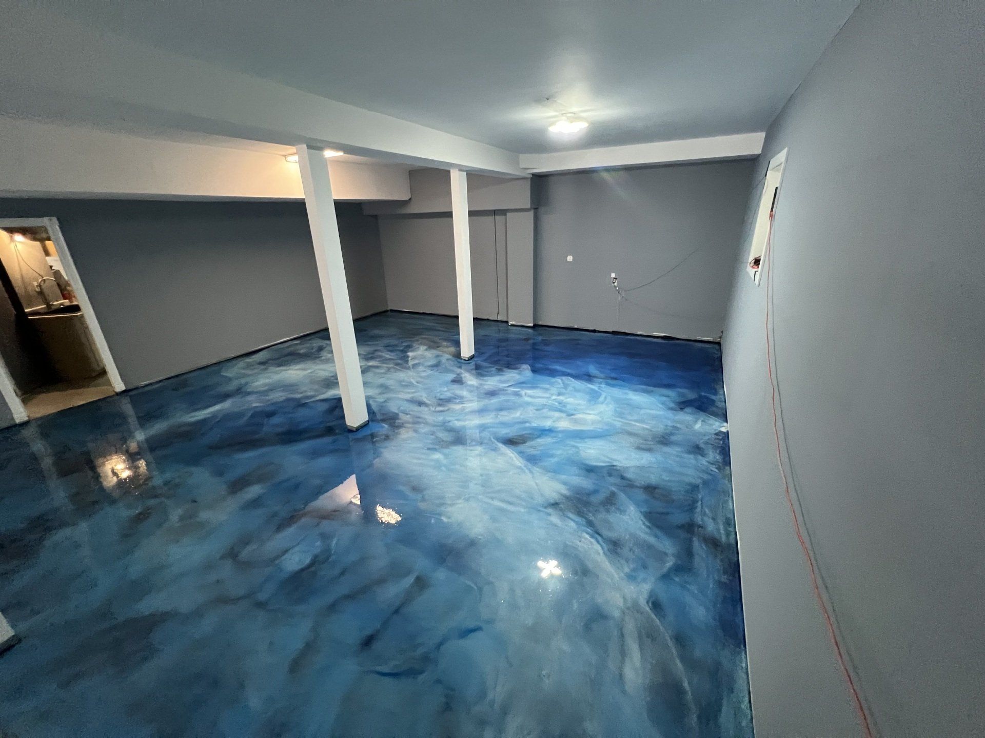 A room with a glossy blue epoxy floor resembling water, gray walls, and white support beams.
