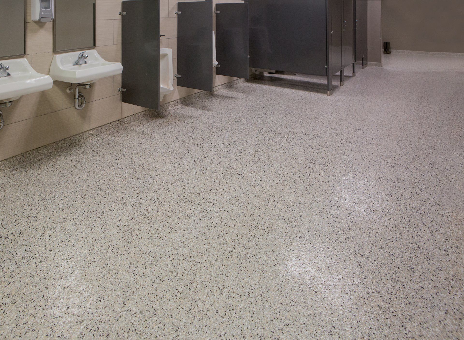 Public restroom with speckled flooring, sinks, and stall dividers. The floor is light with flecks of various dark colors.