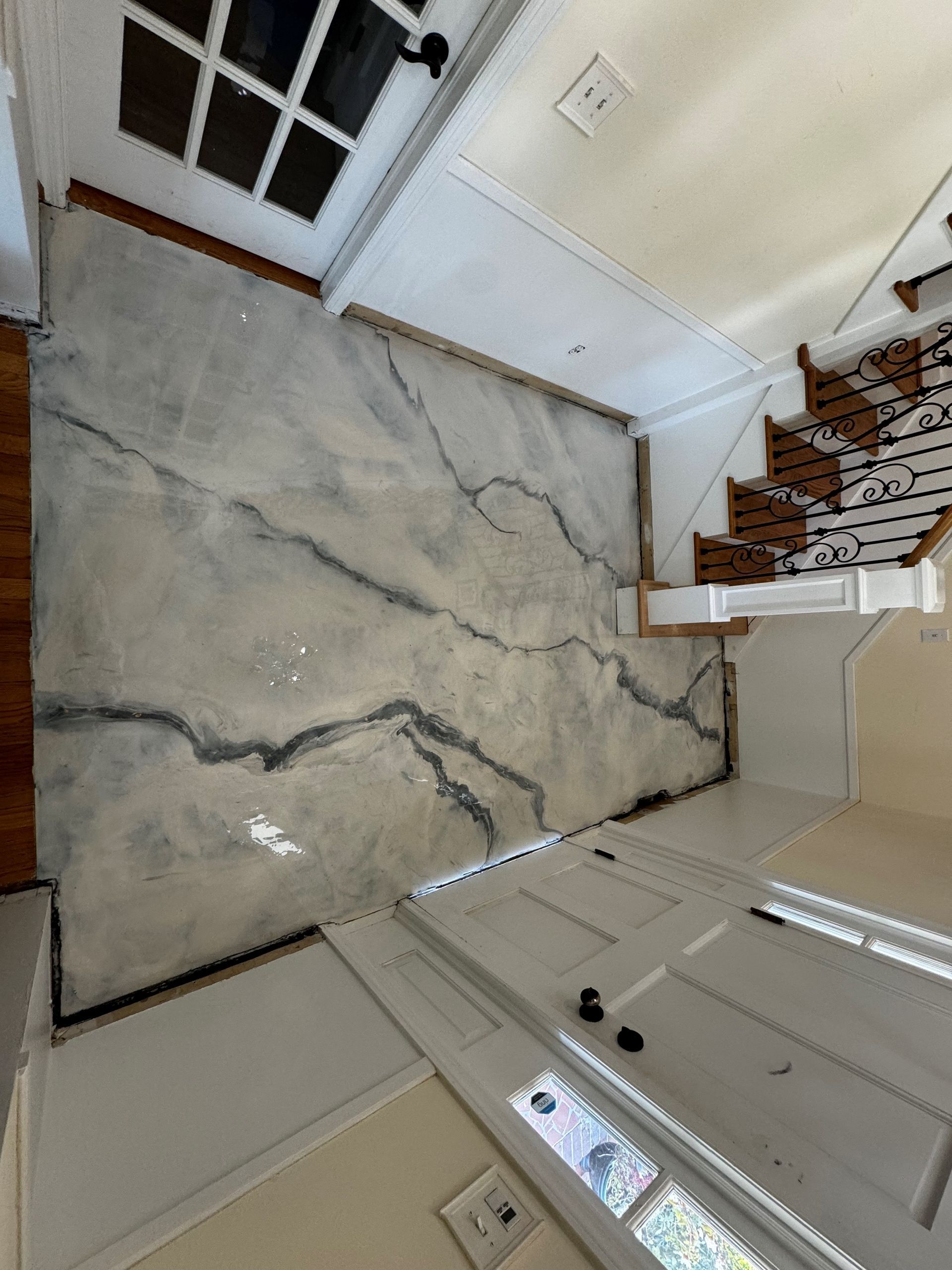 A hallway with a large, decorative concrete floor featuring veining. White trim, a staircase, and an open doorway.