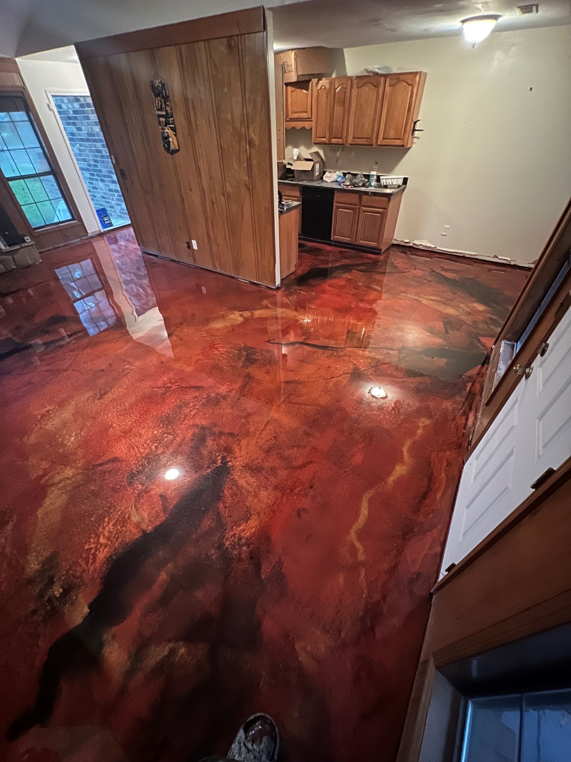 A room with a metallic red and black epoxy floor. The kitchen is visible with wooden cabinets and appliances.
