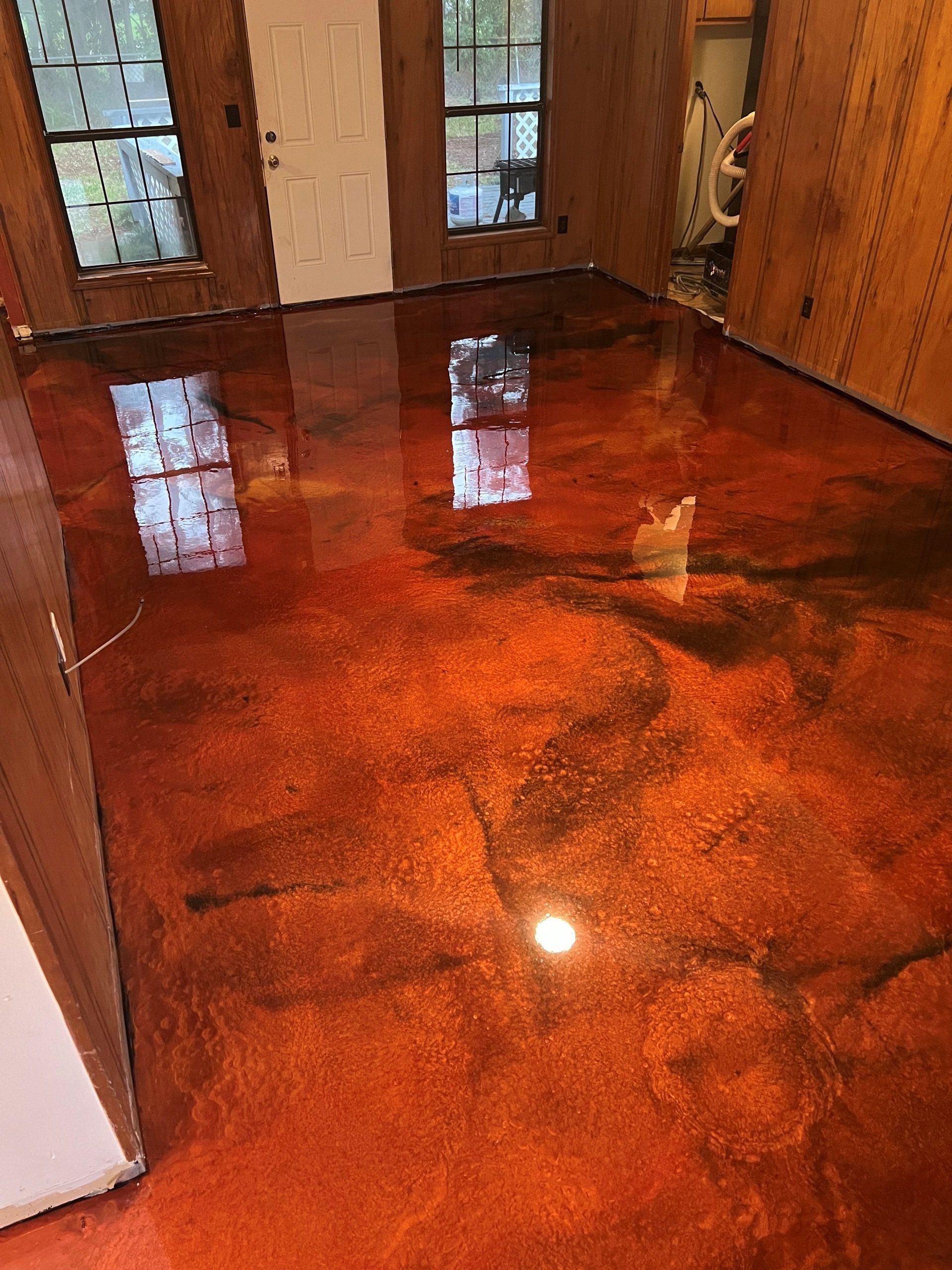 A room with a shiny, orange and black metallic epoxy floor, reflecting the windows, door, and surrounding walls.