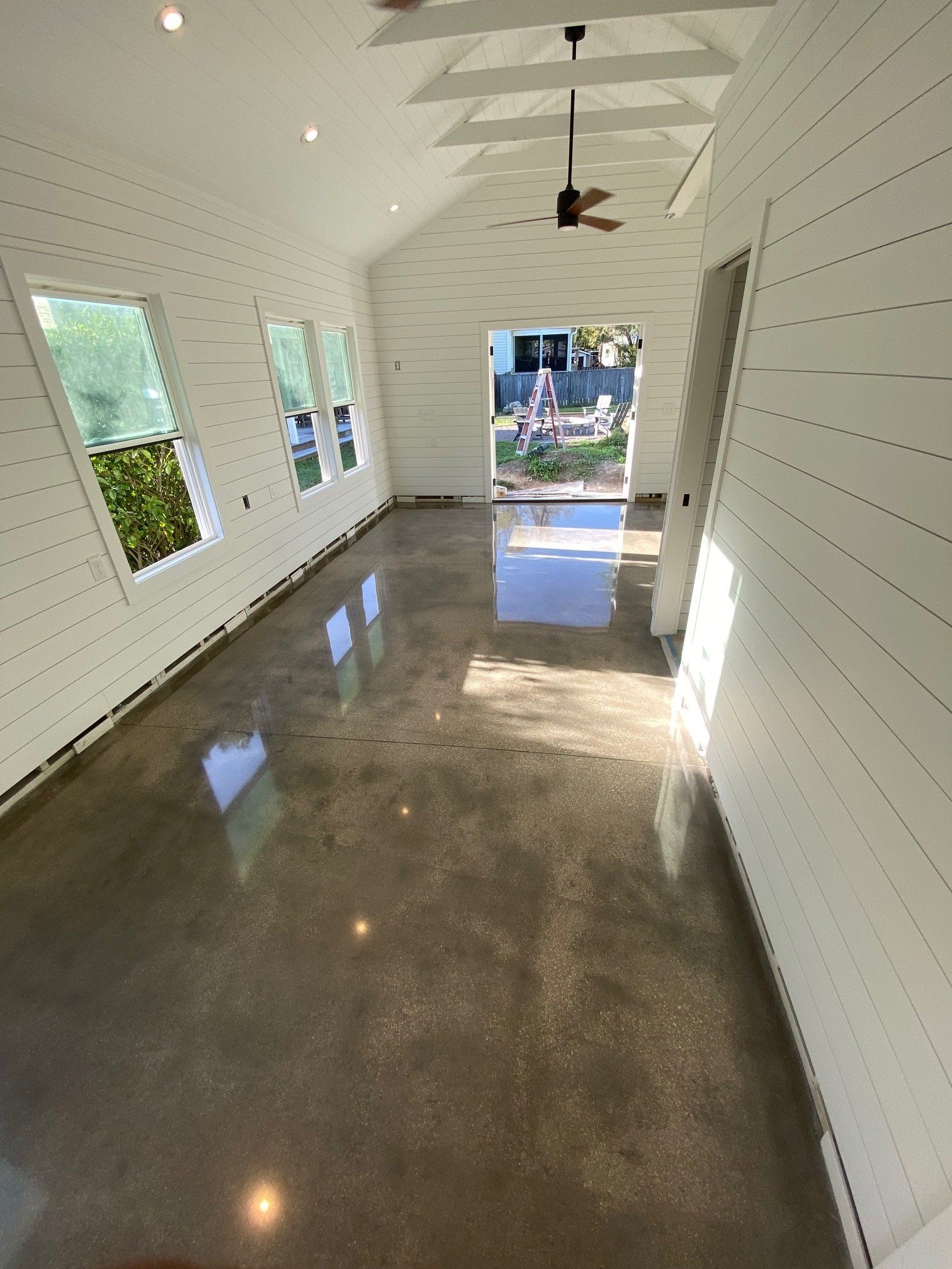 An interior view of a room with a polished concrete floor, white shiplap walls, and an open doorway.
