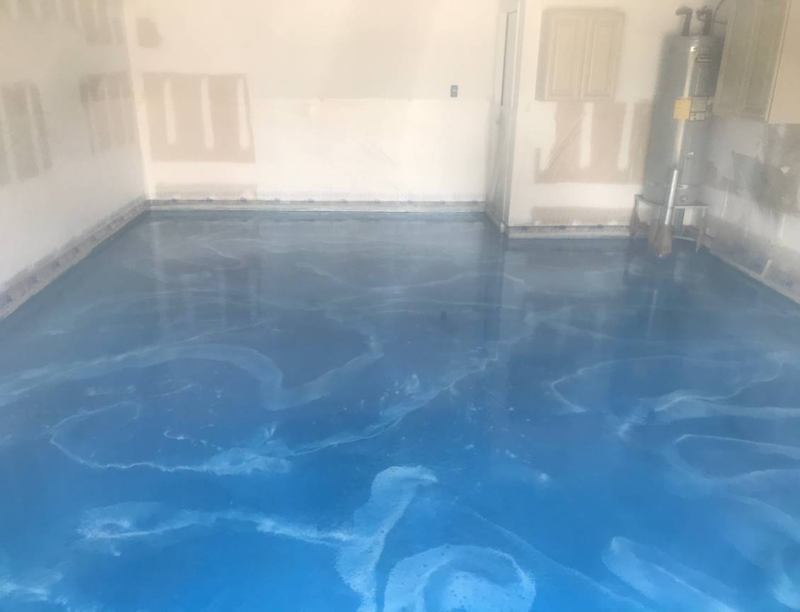 Blue epoxy-coated garage floor with white marbled patterns. The walls are white and unfinished.