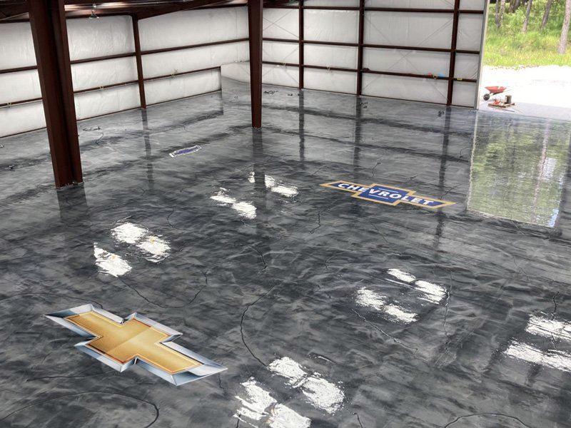 A shiny, metallic epoxy floor with a Chevrolet logo embedded in it. The interior of a metal building reflects light.