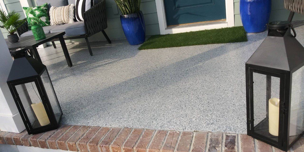 A front porch with a speckled concrete floor, lanterns, and a seating area. Blue pots with plants are seen next to the door.