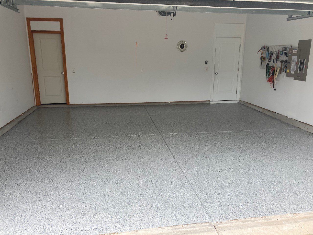 Empty garage with a speckled gray epoxy floor, white walls, and two doors.