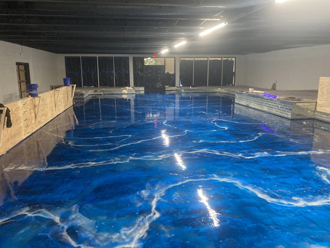 A large room with a glossy blue and white epoxy floor designed to resemble ocean waves; the setting under construction.