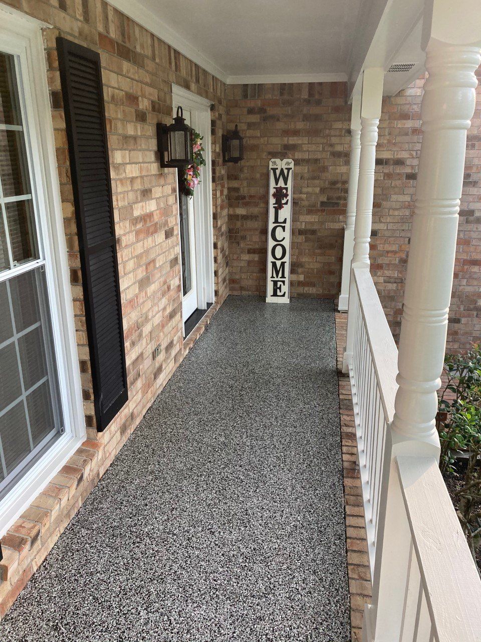 Front porch with speckled gray flooring, brick walls, white pillars and railing, and a