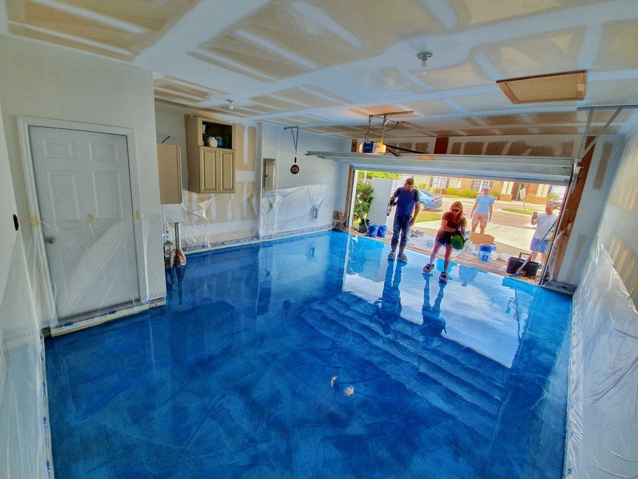 A garage with a vibrant blue epoxy floor; two people stand on it near the open doorway.