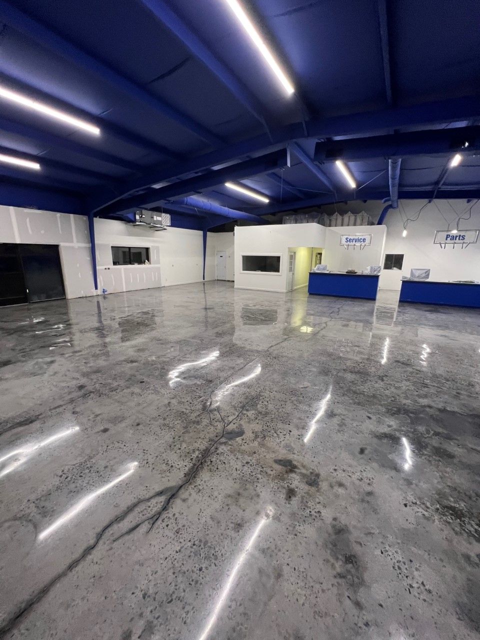 Interior view of a spacious room with a polished concrete floor reflecting overhead lights; walls are white and blue.