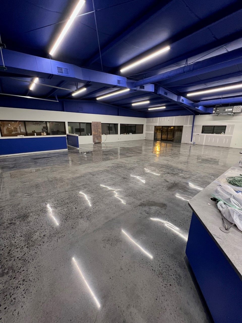 An empty commercial space with a polished concrete floor, blue ceiling and accents. Bright overhead lights reflect.