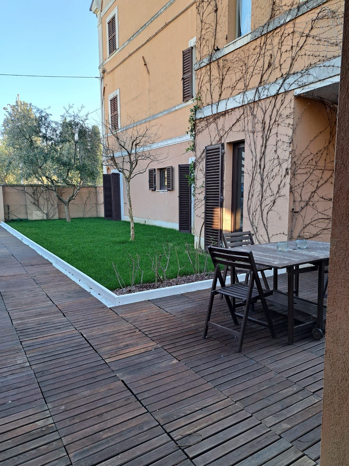 Una terrazza di legno con tavolo e sedie di fronte a un edificio.