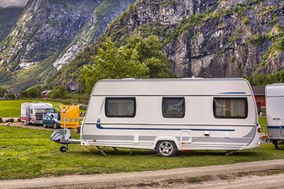 A caravan is parked in a grassy field with mountains in the background.