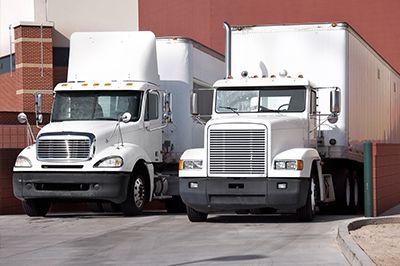 Two white semi trucks are parked next to each other in front of a building.