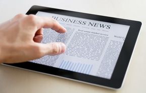 A person is pointing at a business news article on a tablet.