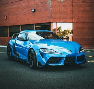 A blue sports car is parked in front of a brick building.