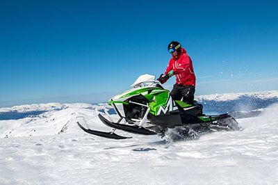 A man is riding a snowmobile on top of a snow covered mountain.