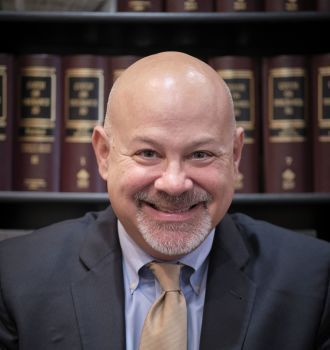 A man in a suit and tie is smiling in front of a bookshelf