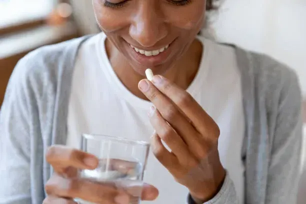 A woman is taking a pill from a glass of water.