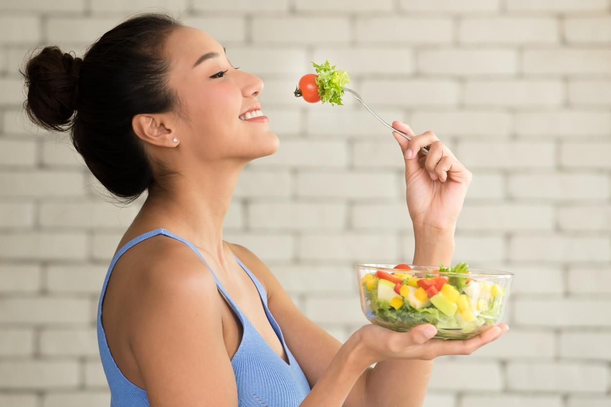 A woman is eating a salad with a strawberry in the air.
