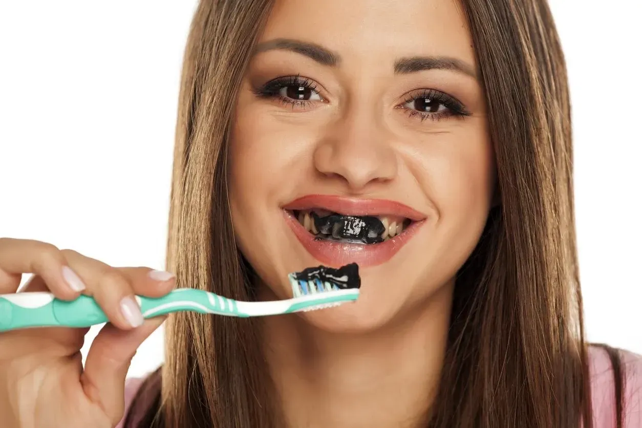 A woman is brushing her teeth with black toothpaste.