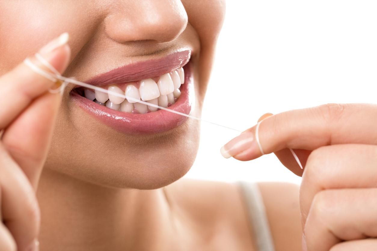 A woman is flossing her teeth with a dental floss.