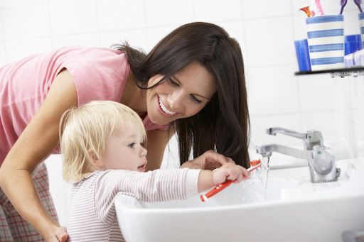 A woman and a child are brushing their teeth in a bathroom sink.