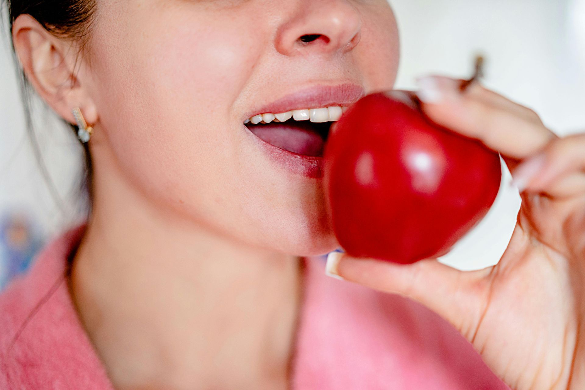Close-up of a person about to bite a shiny red apple.