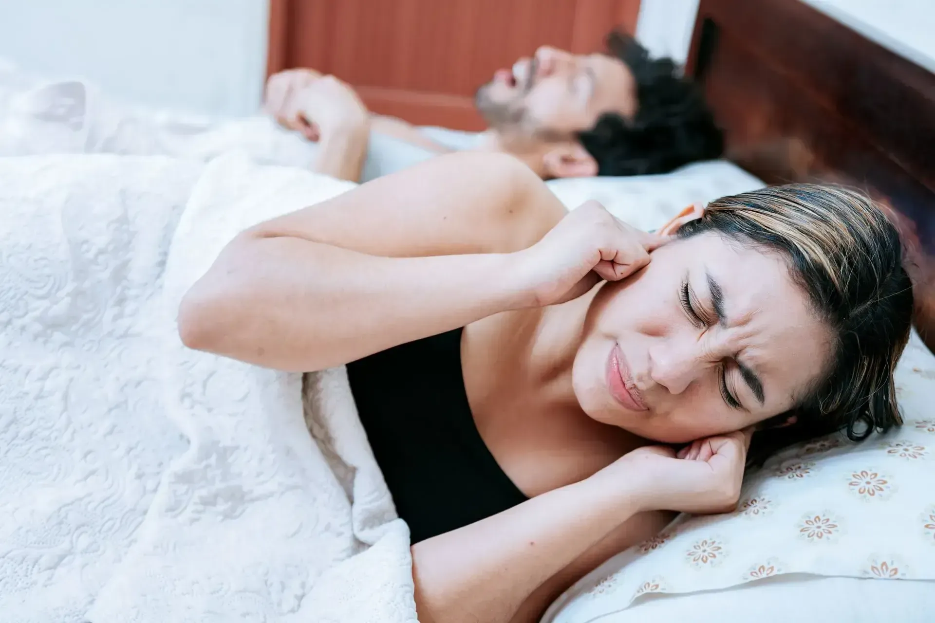 a woman lying in bed plugging her ears trying to sleep