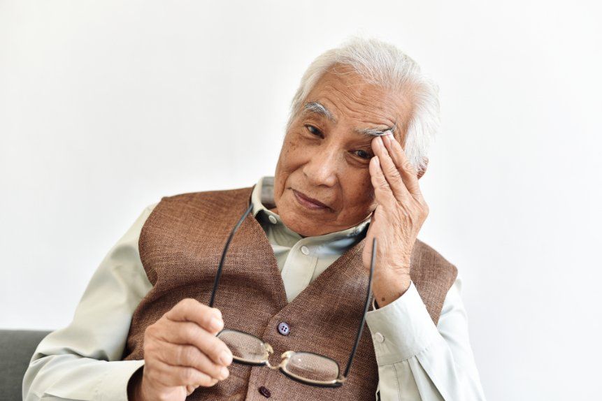 An elderly man wearing glasses is rubbing his forehead.