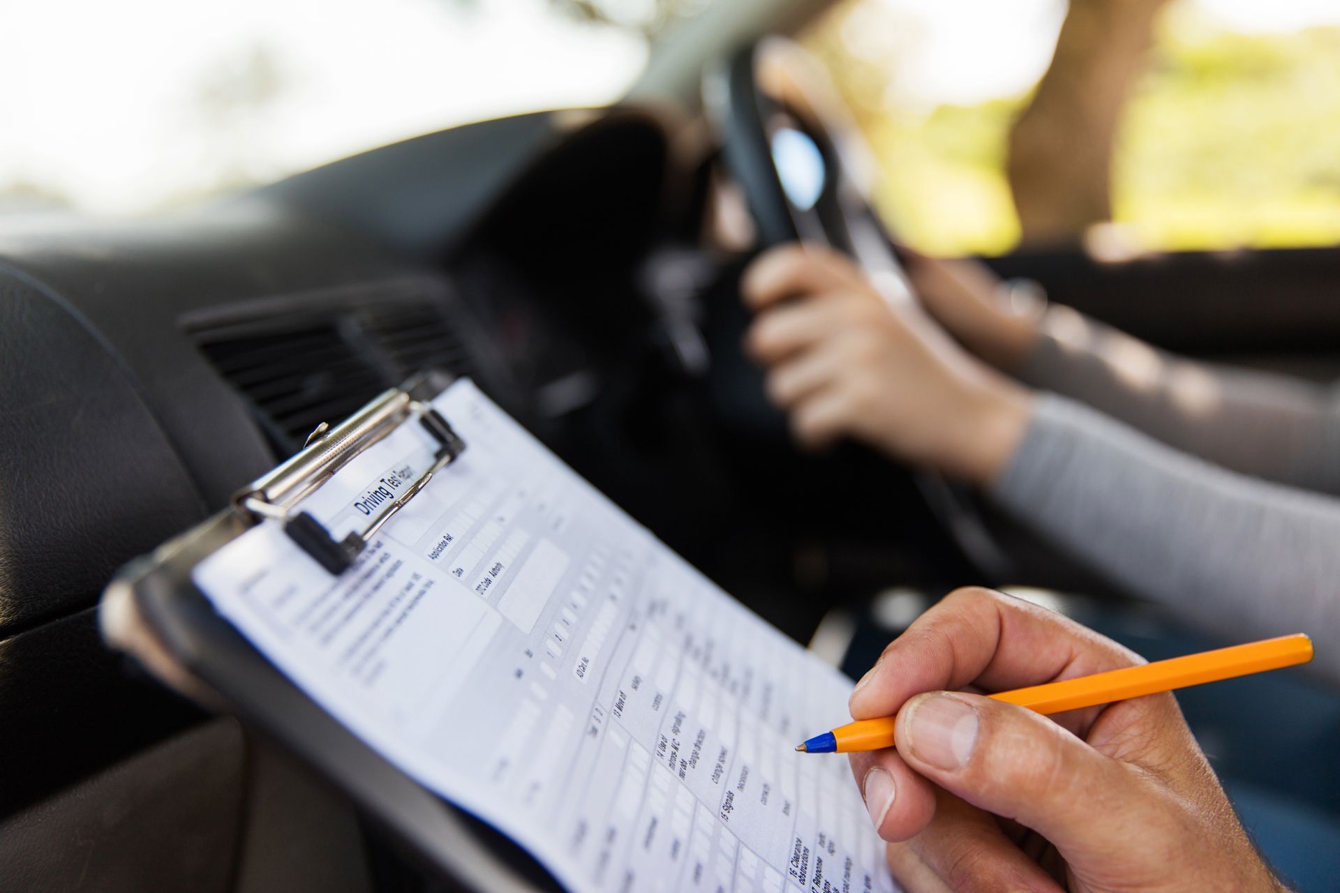 A person is taking a driving test in a car and writing on a clipboard
