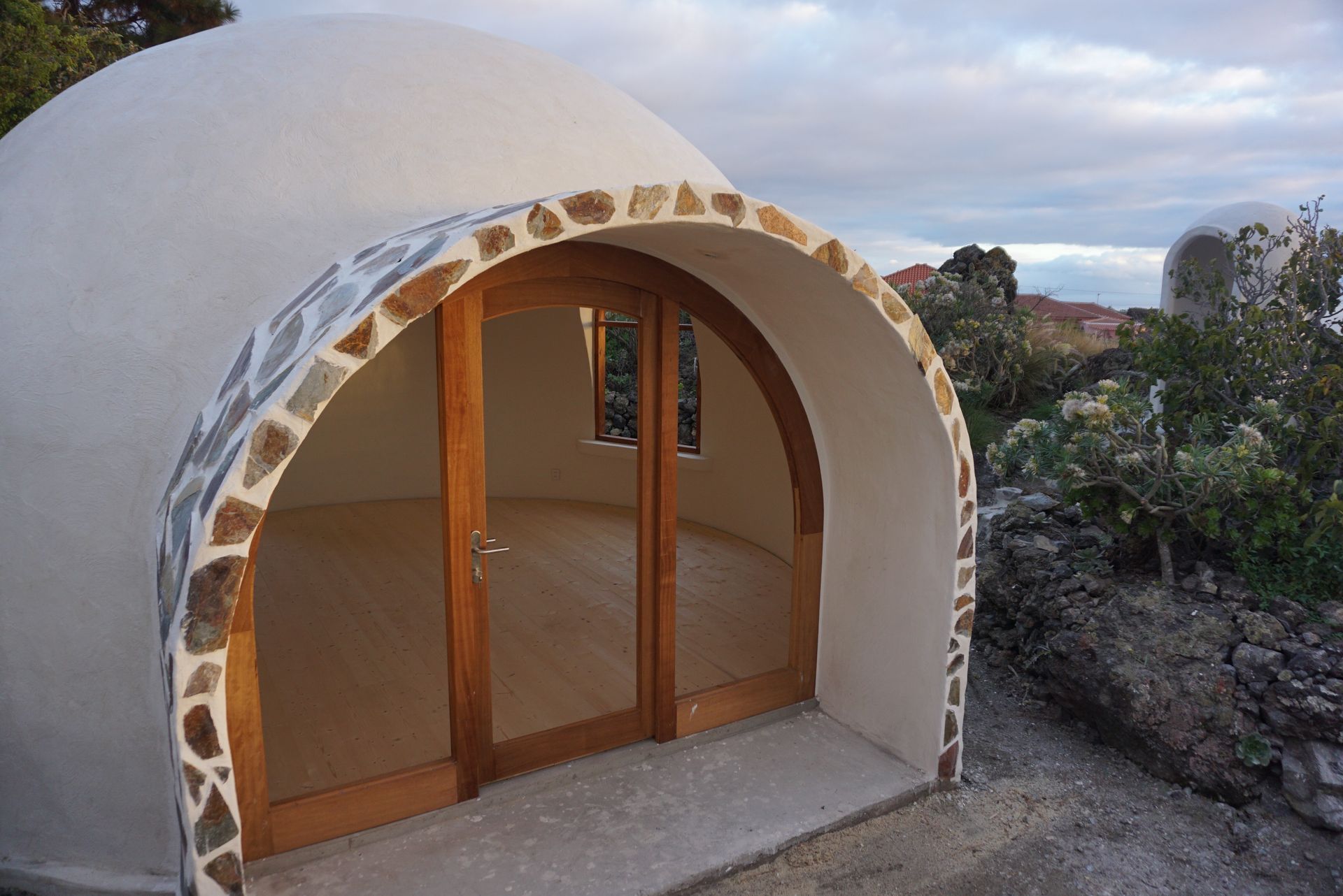 Aircrete dome seen from the front with off-white plaster exterior and arched glass front door.