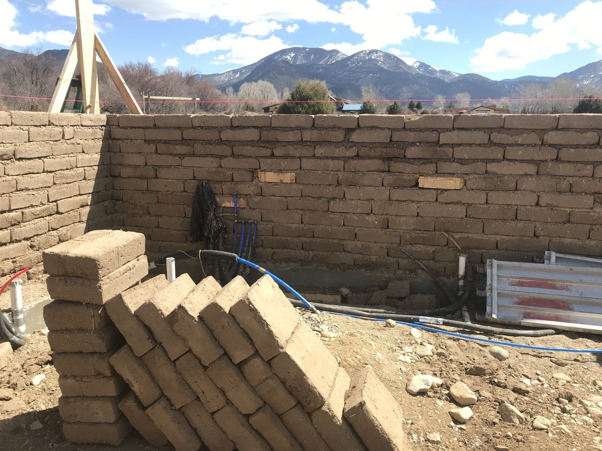 A half formed adobe brick wall with a stack of adobe bricks ready to be used .