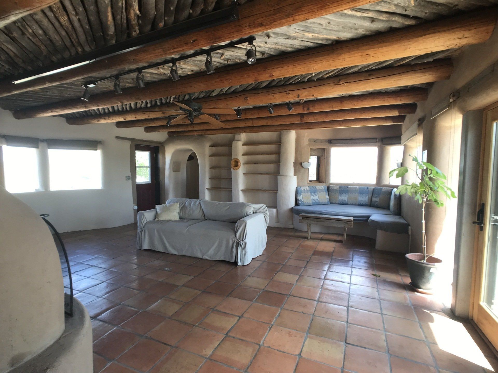 Interior of an adobe brick home with saltillo tiled floors, wooden ceiling (vigas and latias), lots of windows and a built in banco (sofa) as well as a regular sofa in the middle of the living room.