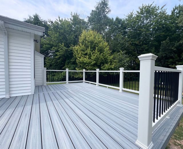 A large gray deck with a white railing and trees in the background.