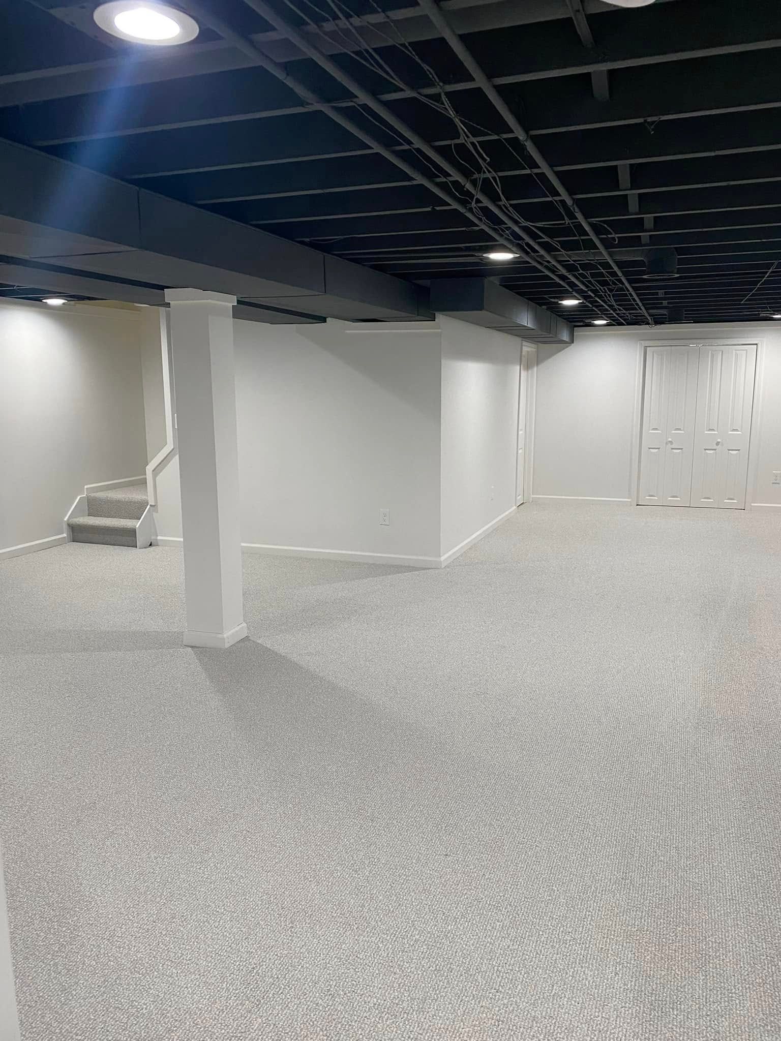 An empty basement with white walls and a black ceiling.