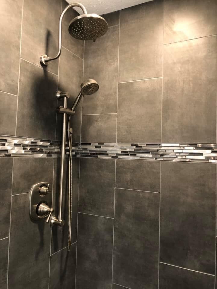 A shower with a stainless steel shower head and a tiled wall.