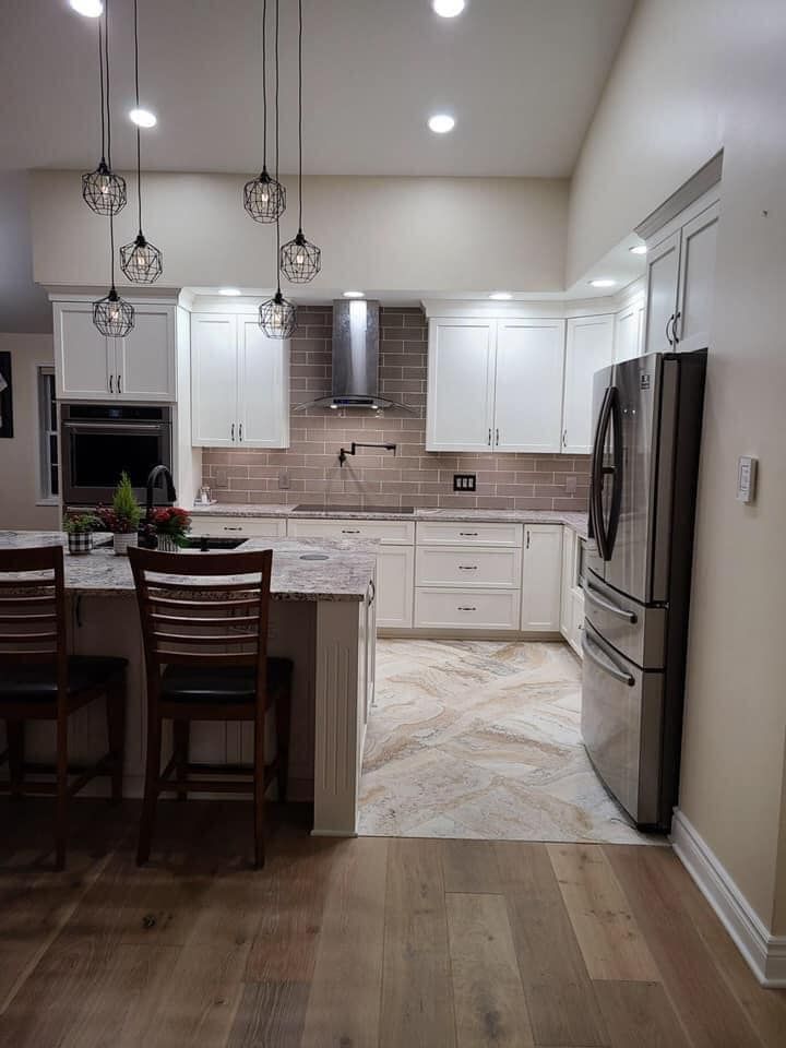 A kitchen with white cabinets , stainless steel appliances , hardwood floors and a refrigerator.