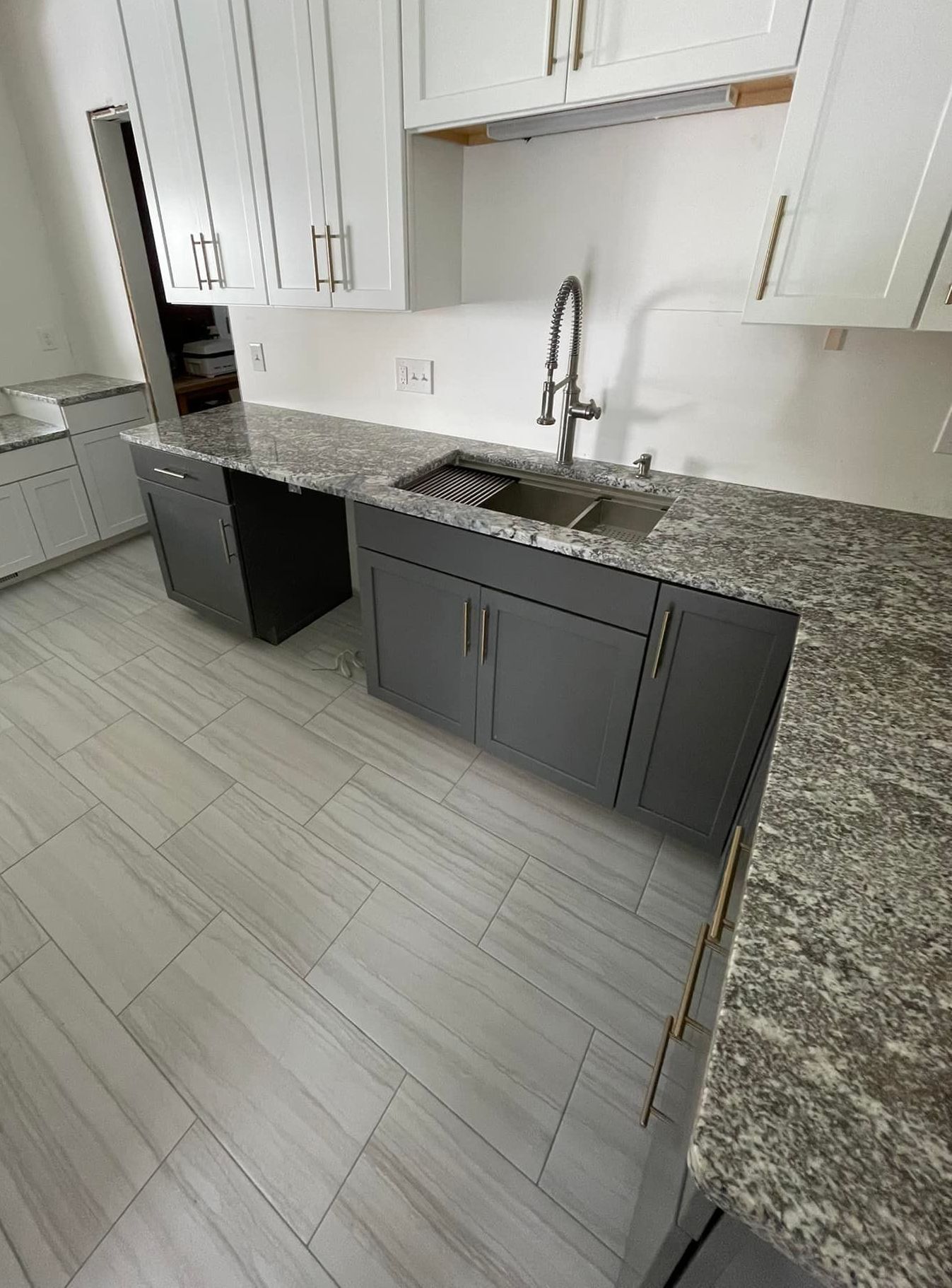 A kitchen with granite counter tops , gray cabinets and a sink.