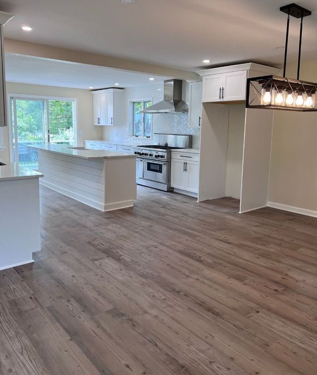 An empty kitchen with hardwood floors and white cabinets.