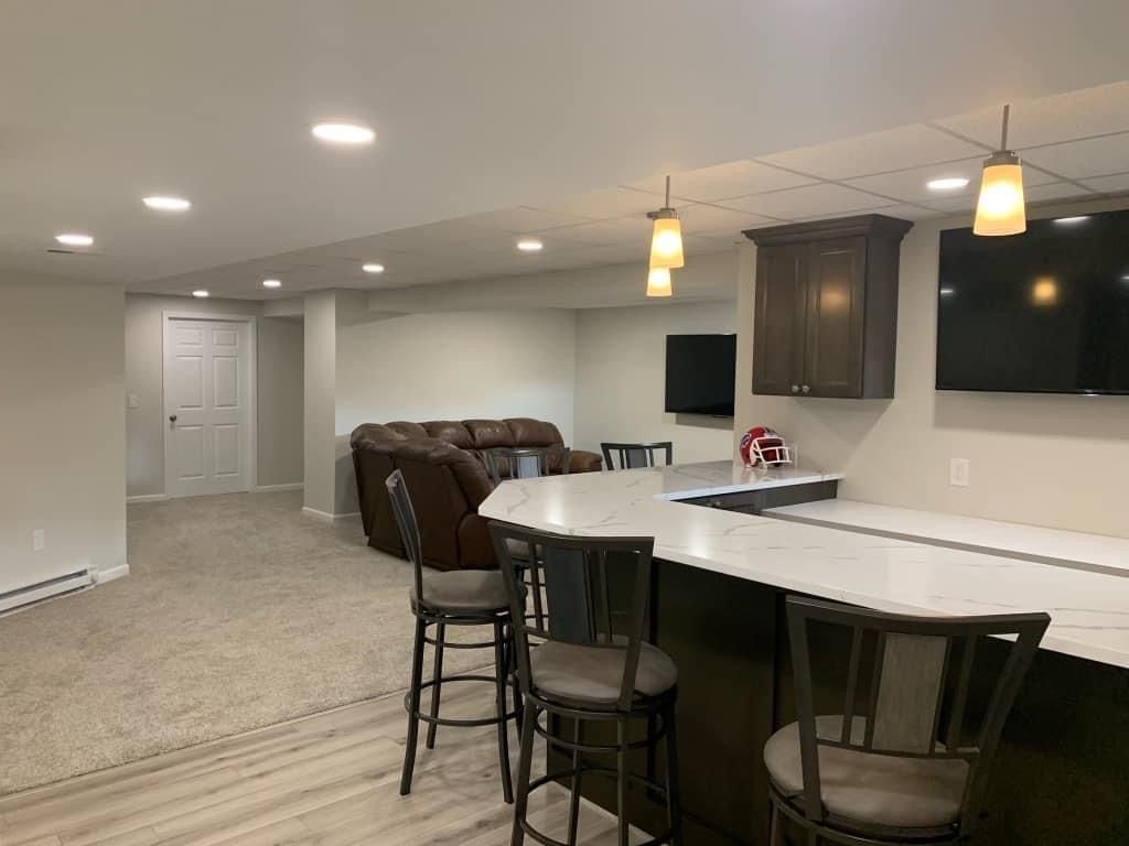 A basement with a bar , chairs , a couch and a television.