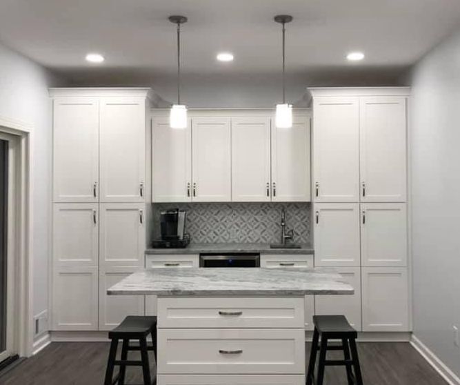 A kitchen with white cabinets , a large island , and stools.