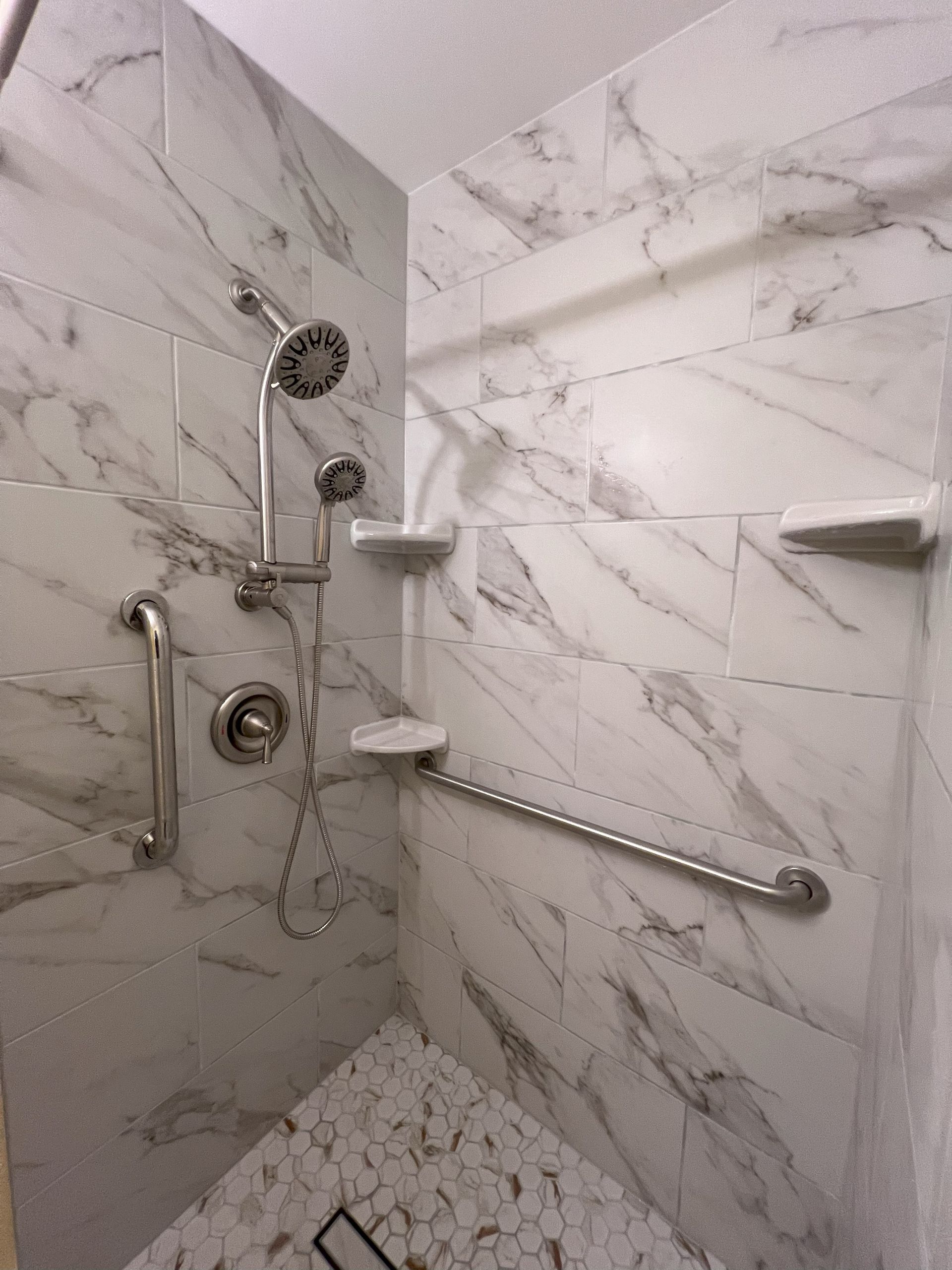A walk in shower with marble tiles and a hand rail.