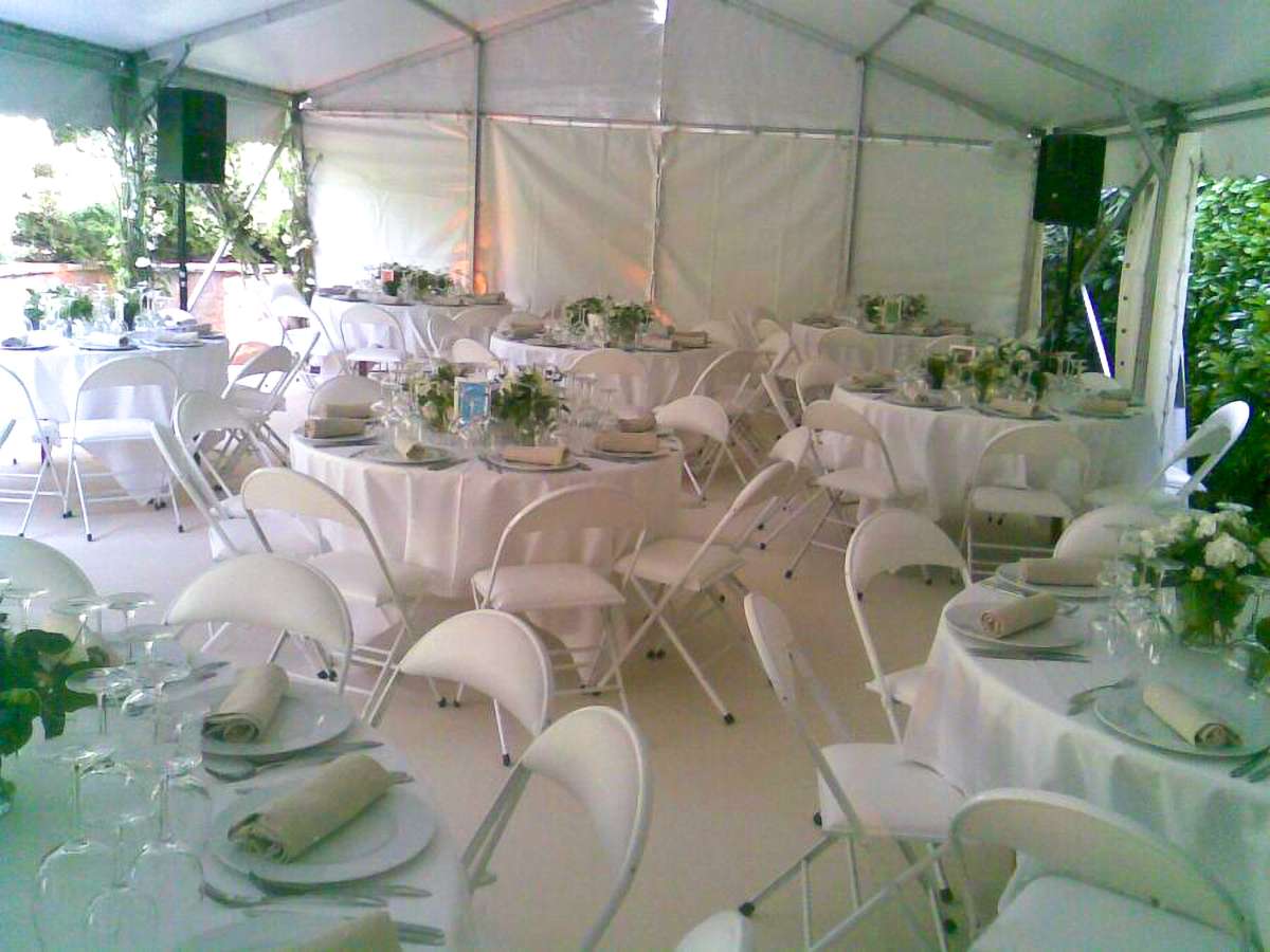 Overall view under a tent arranged for a wedding with several tables and white chairs