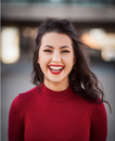 A woman in a red sweater is smiling and wearing red lipstick.