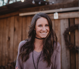 A woman wearing a choker is smiling in front of a wooden fence.