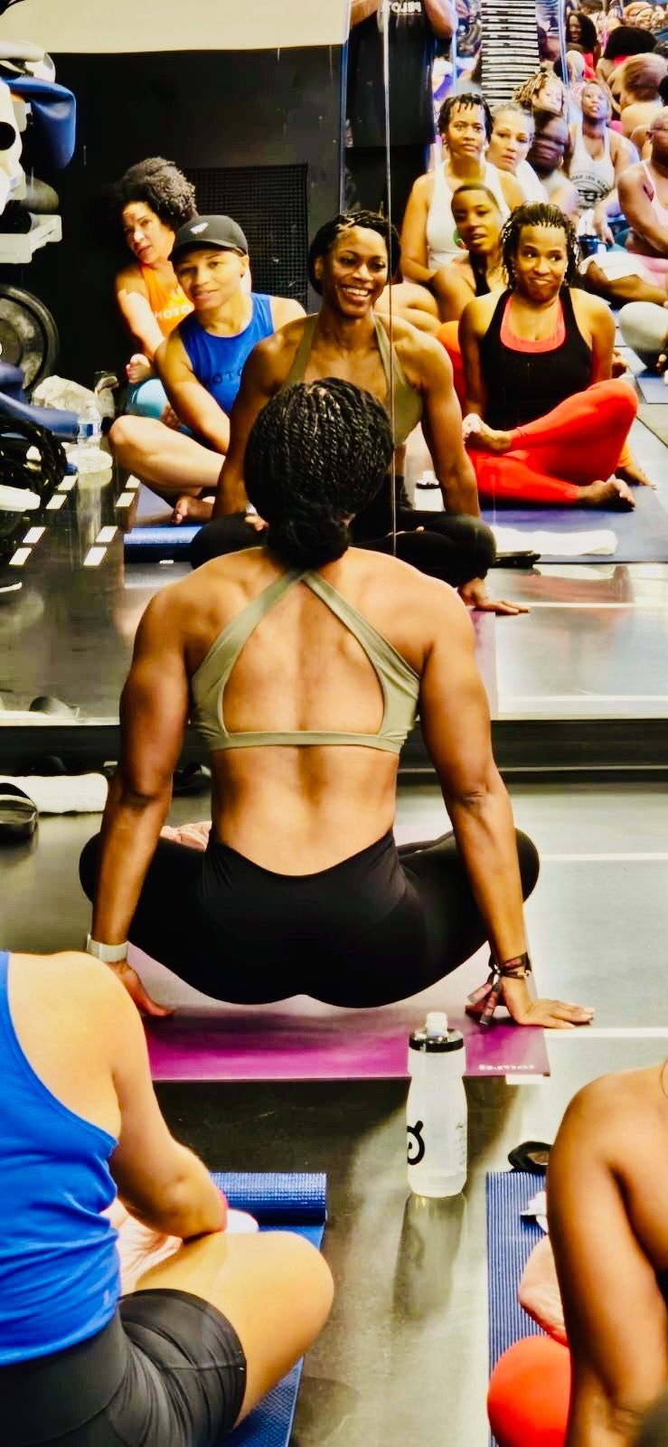A group of people are sitting on yoga mats in front of a mirror in a gym.