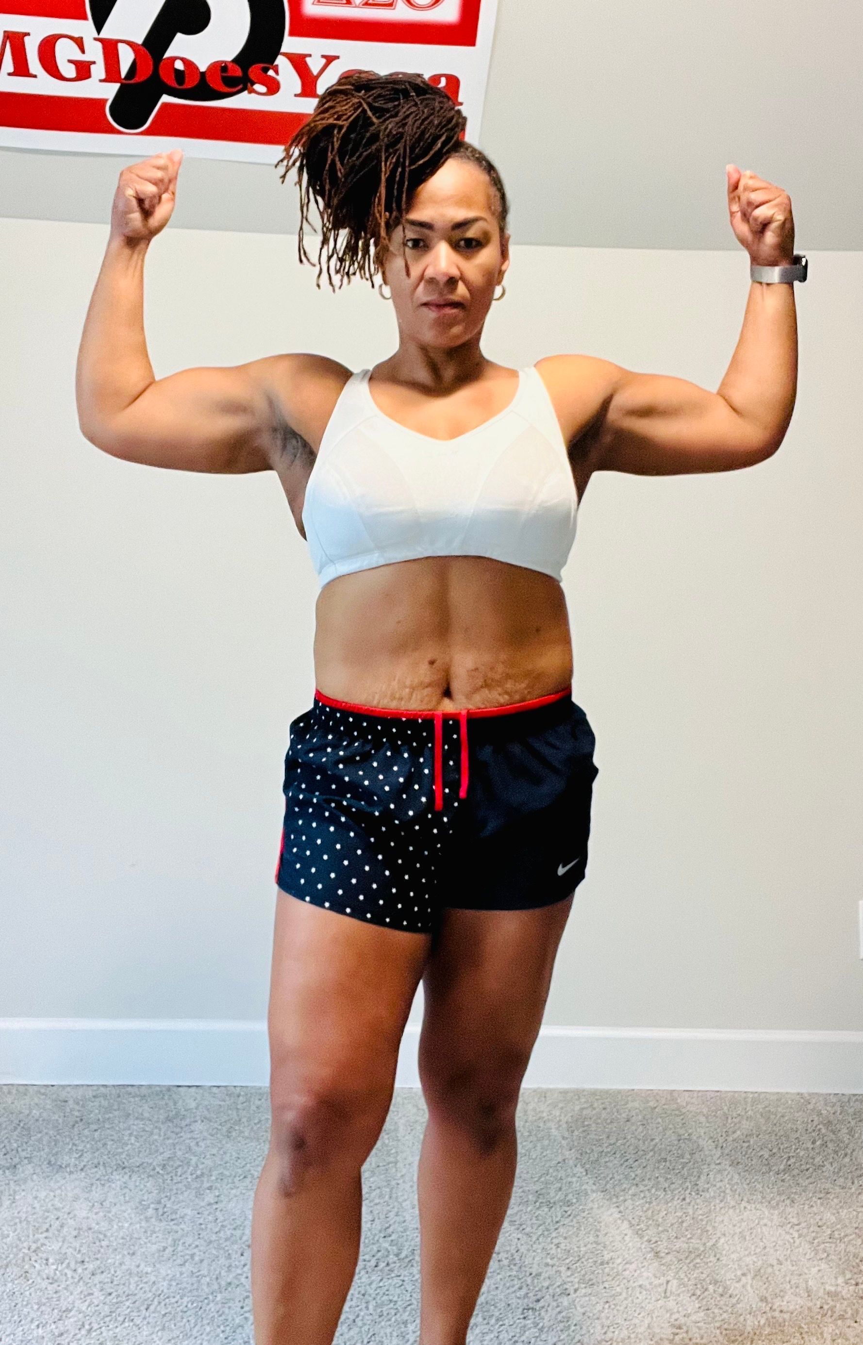 A woman is flexing her muscles in front of a gym sign.