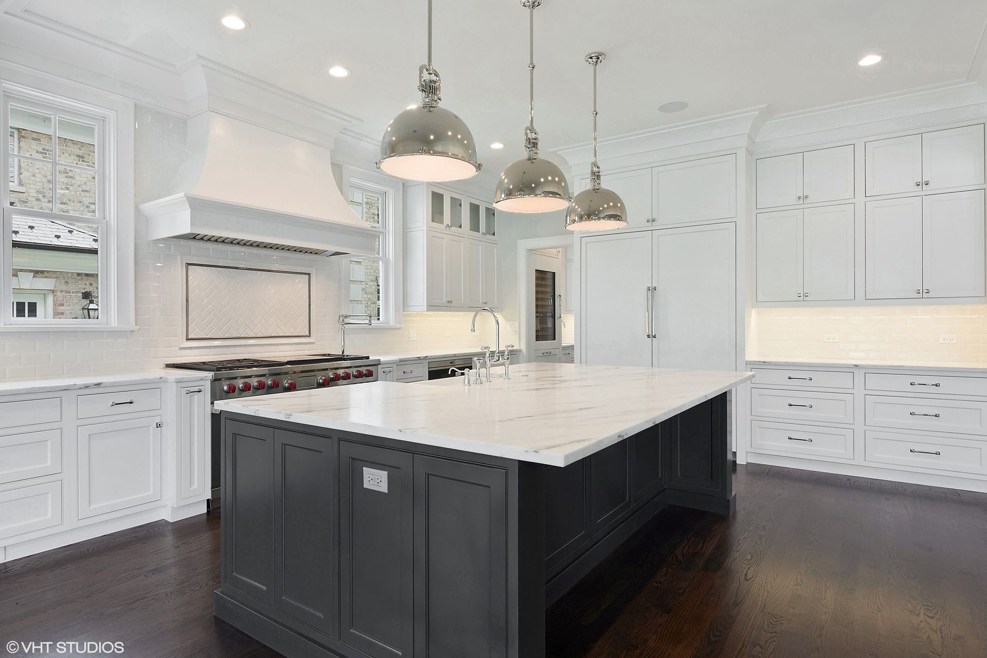 A modern kitchen and dining area featuring a light wood table, black Eames-style chairs, and dark wood cabinets.